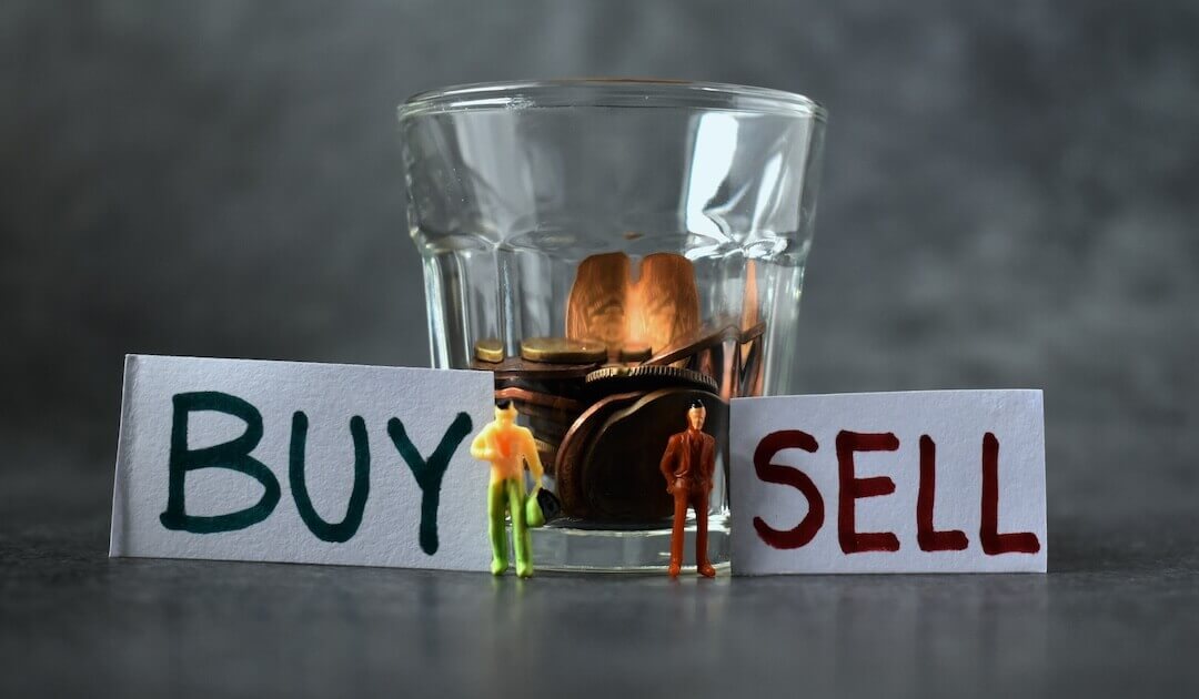 miniature models placed side by side to signs of Buy and Sell with a glass of coins