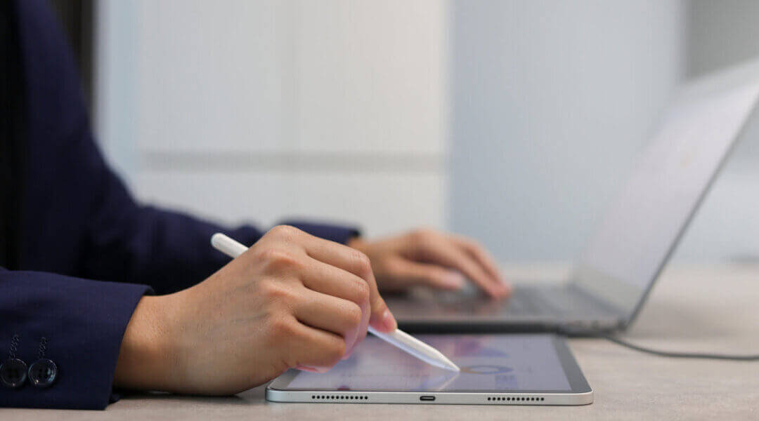 close up of person's hand using stylus pen to write or check summary profit report and performance of company financials in office on a desk