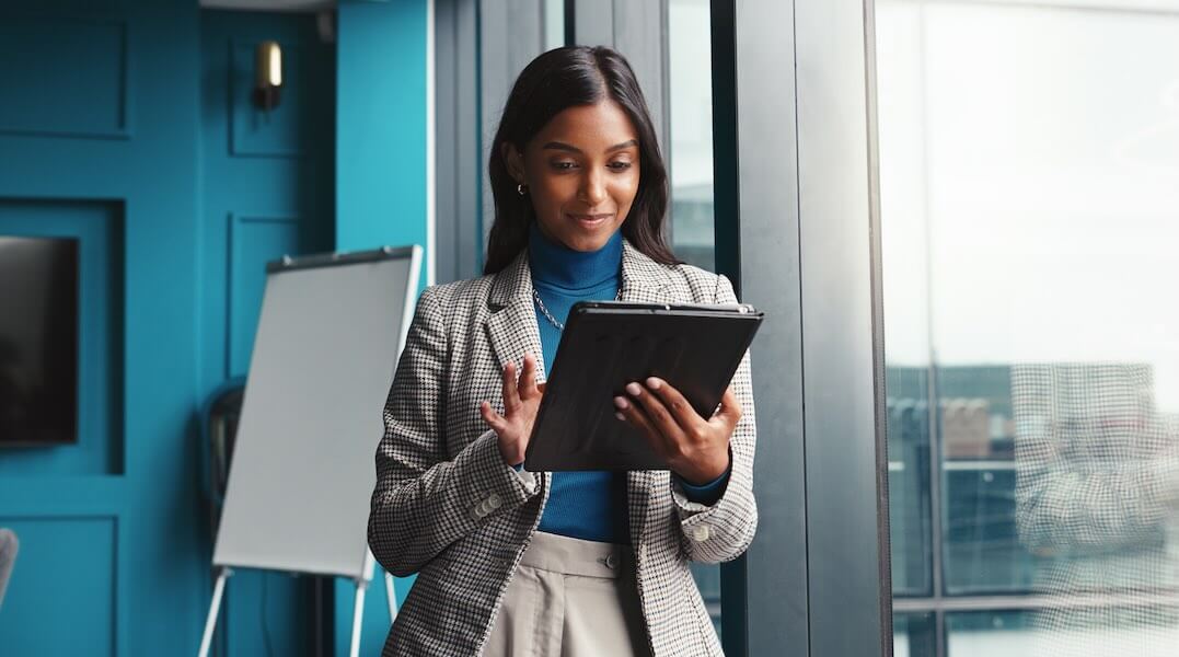 Business woman stands next to large window looking at tablet