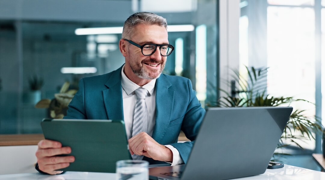 Business owner reviewing financial reports on a laptop and tablet at his desk